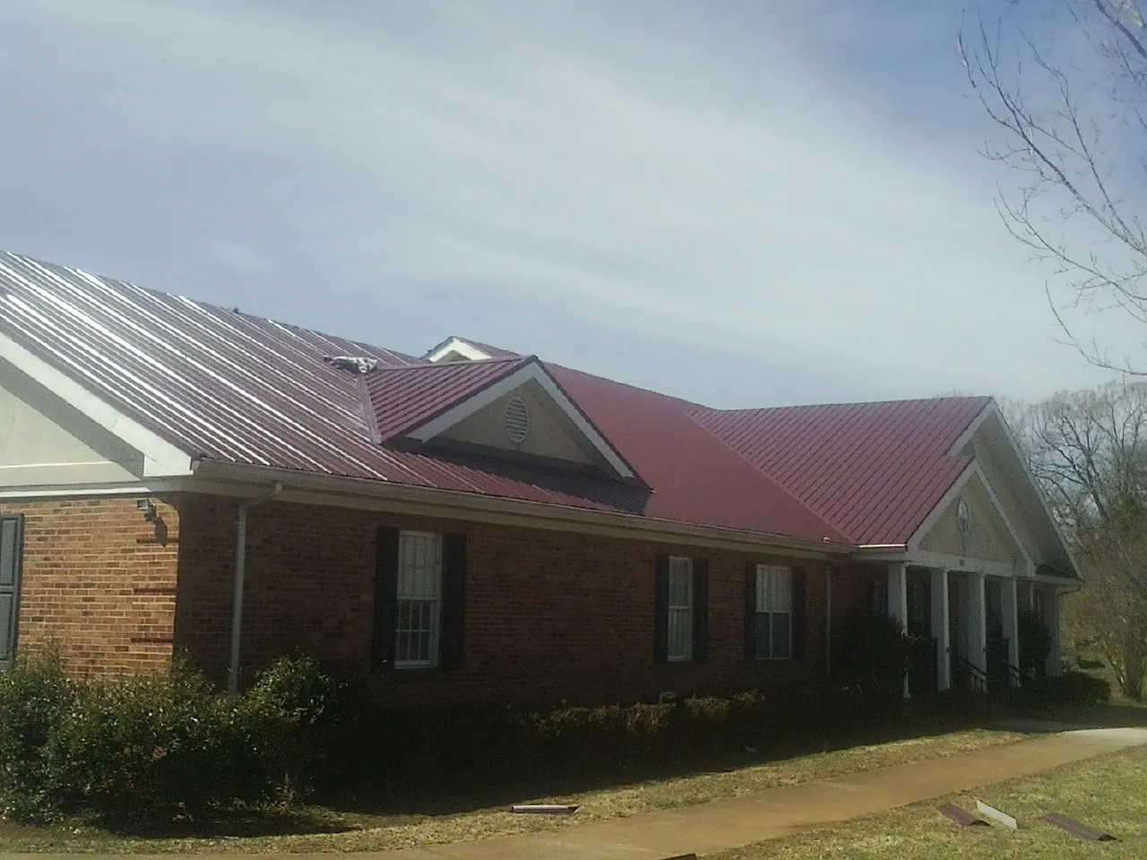 Red metal roof with gabled entries on a long brick building, from a Hail Damage Roof Repair job in Baileyton