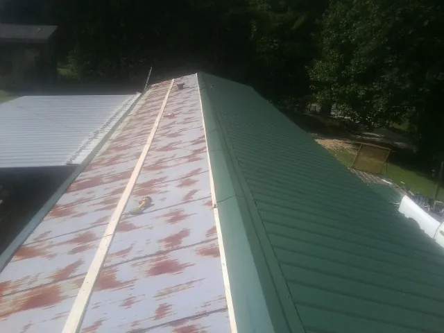 Old rusted panels beside newly installed green metal roofing — Wind Damage Roof Repair by Roofing Brothers in Baileyton