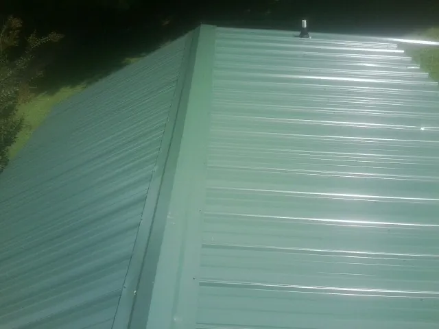 New green metal panels meeting at the ridge of a roof — Flat Roof Repair work by our crew in Baileyton