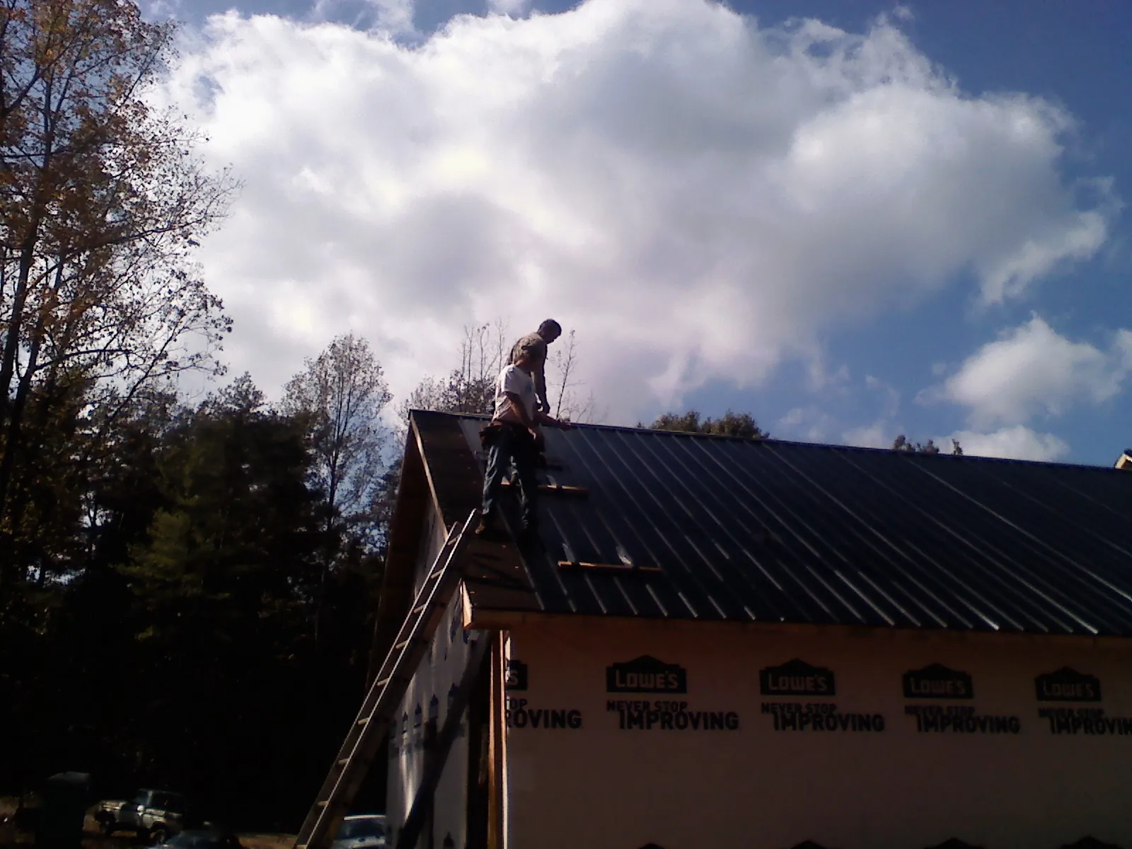 Roofer fastening dark metal panels high against a cloudy sky, from a Roof Inspection job in Baileyton