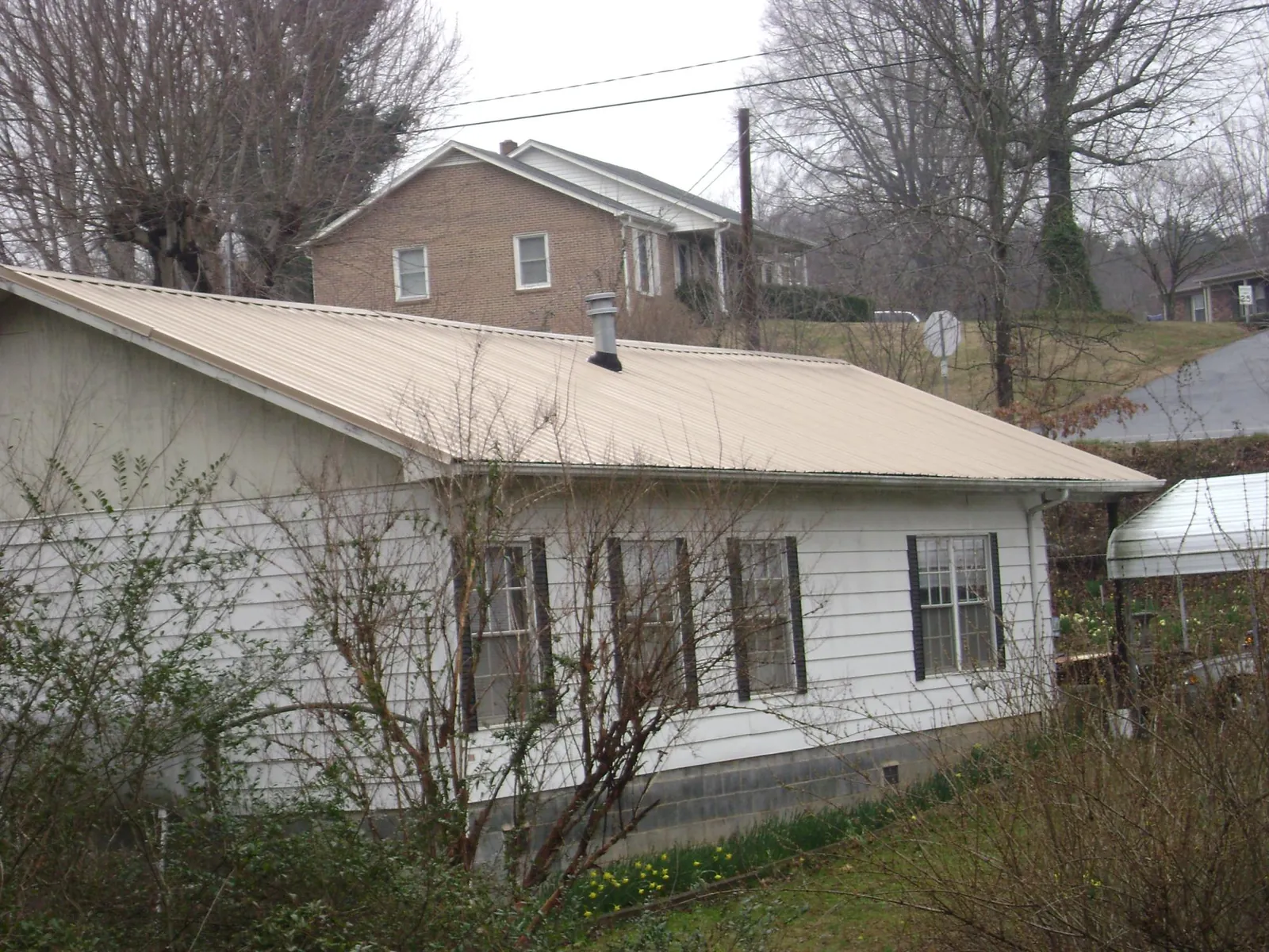 Tan metal roof on a white sided house set into a hillside — Commercial Roofing by Roofing Brothers in Baileyton