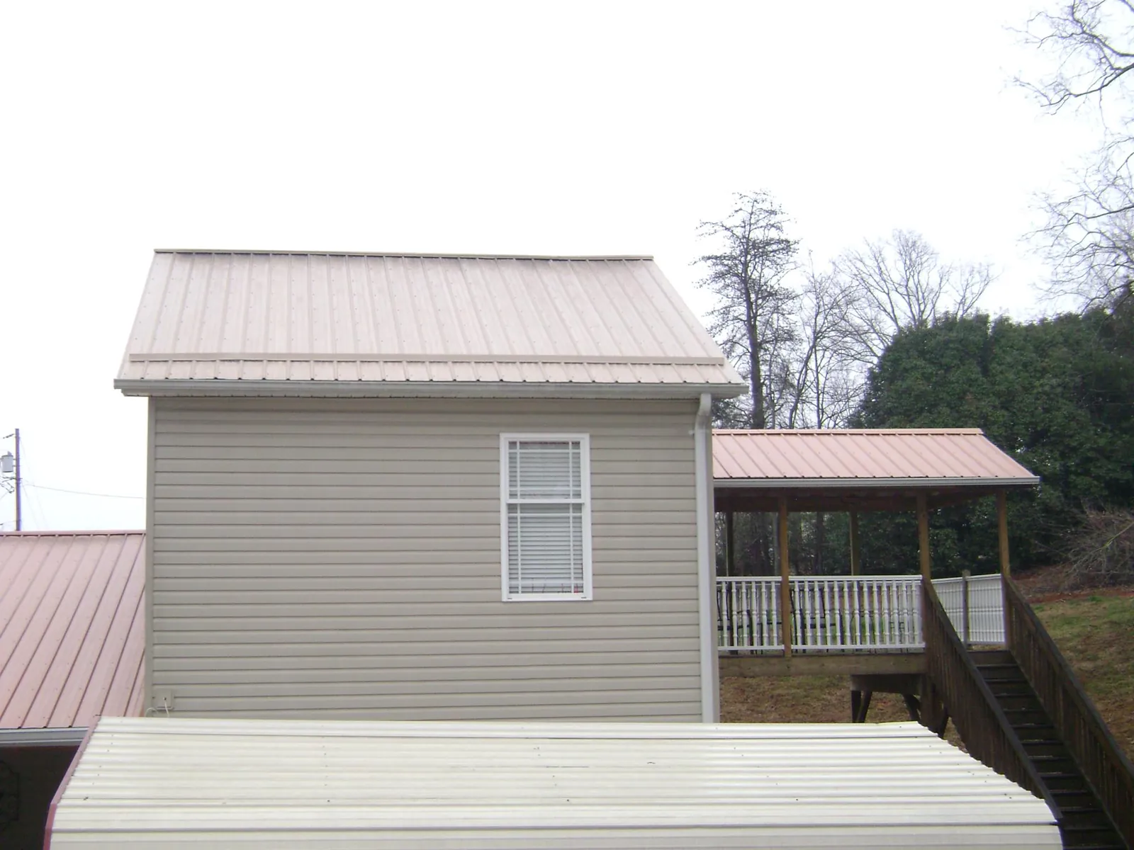 Tan metal roofs on a two story addition and attached porch, from a Roof Replacement job in Baileyton